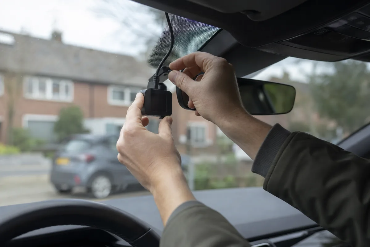 Handen die een dashcam achter de binnenspiegel op de voorruit bevestigen