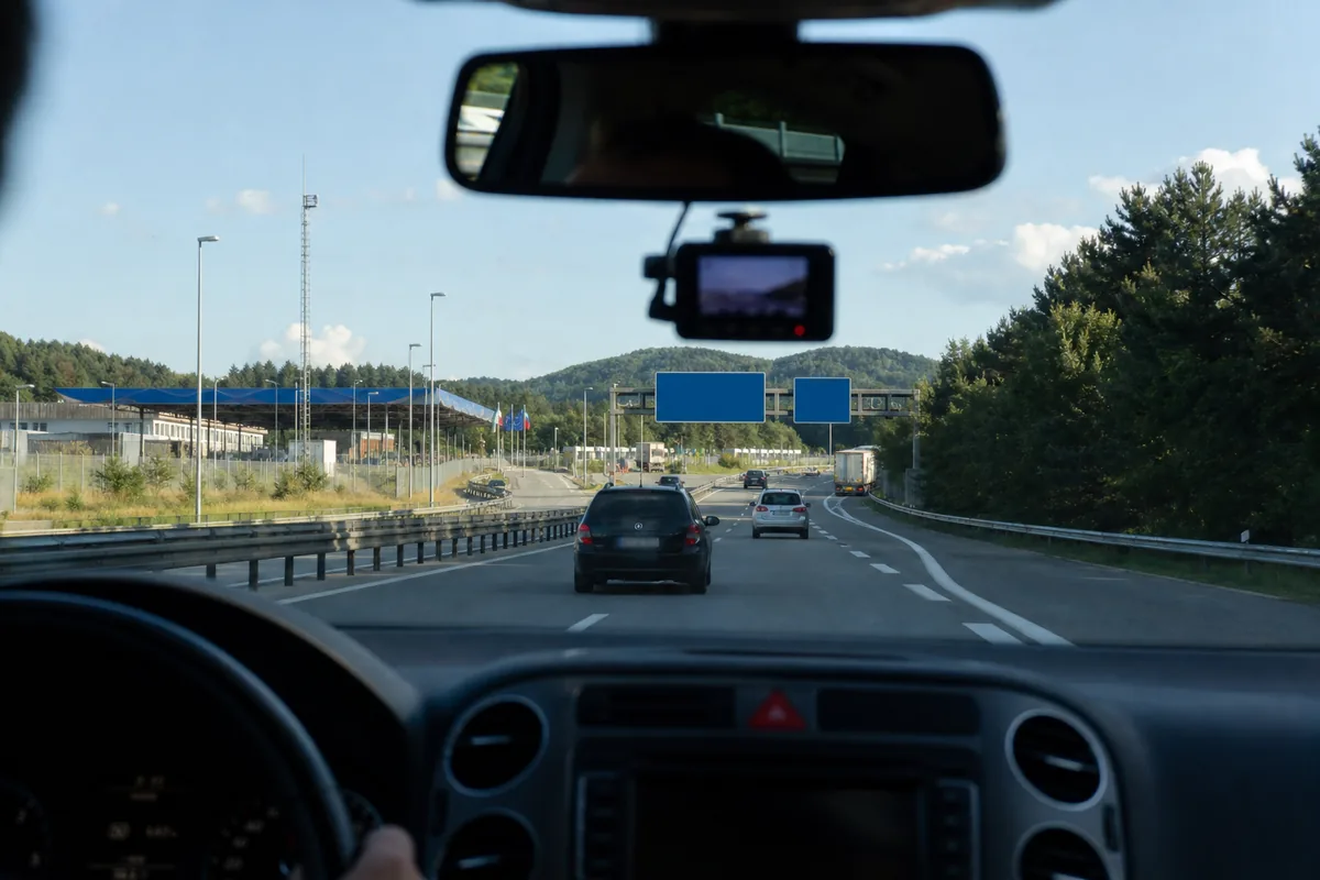 Zicht vanuit de auto op een Europese snelweg richting de grens, met een dashcam achter de spiegel